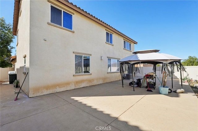 rear view of house featuring stucco siding, a tile roof, a patio, fence, and a gazebo