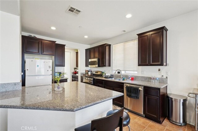 kitchen with visible vents, stone countertops, a sink, stainless steel appliances, and dark brown cabinets