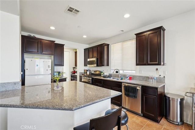 kitchen featuring visible vents, stone countertops, a sink, stainless steel appliances, and dark brown cabinetry