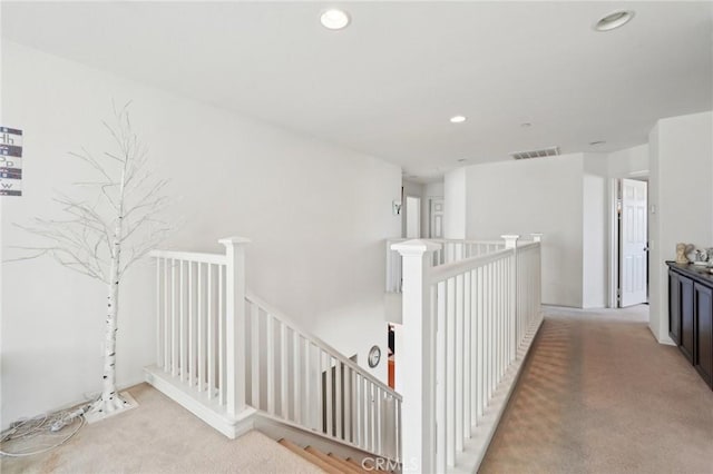 hall with an upstairs landing, visible vents, carpet flooring, and recessed lighting