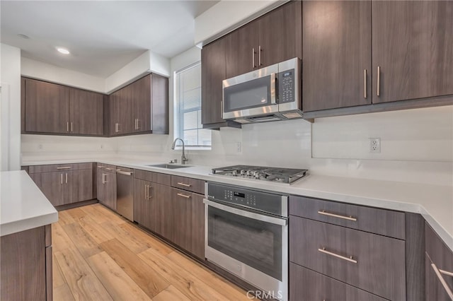 kitchen with a sink, light wood-type flooring, dark brown cabinetry, light countertops, and appliances with stainless steel finishes