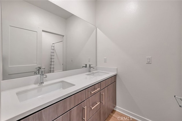 bathroom with baseboards, wood finished floors, double vanity, and a sink