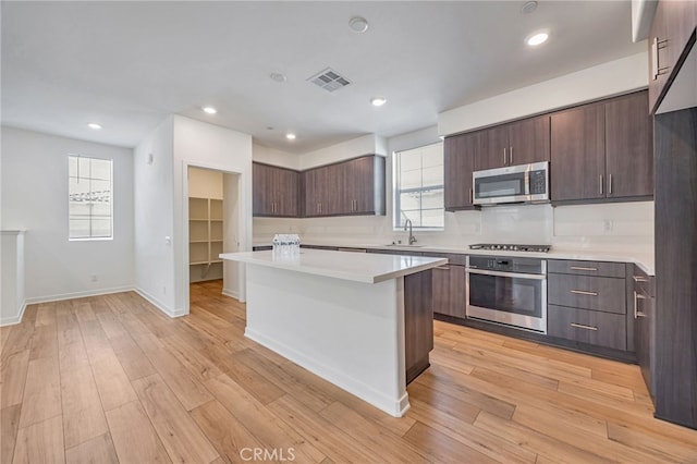 kitchen featuring light wood-style flooring, appliances with stainless steel finishes, light countertops, a kitchen island, and dark brown cabinets