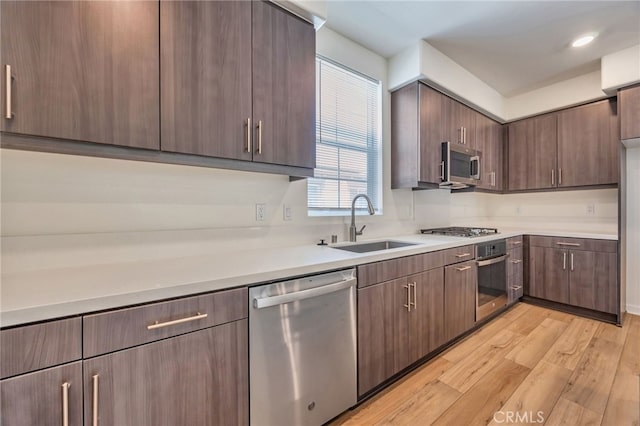 kitchen with light wood-style floors, appliances with stainless steel finishes, light countertops, and a sink