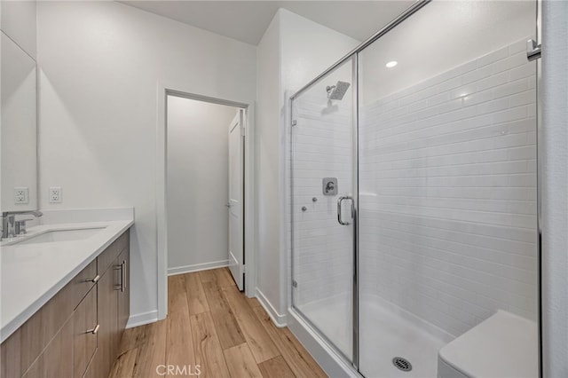 bathroom featuring wood finished floors, vanity, a stall shower, and baseboards