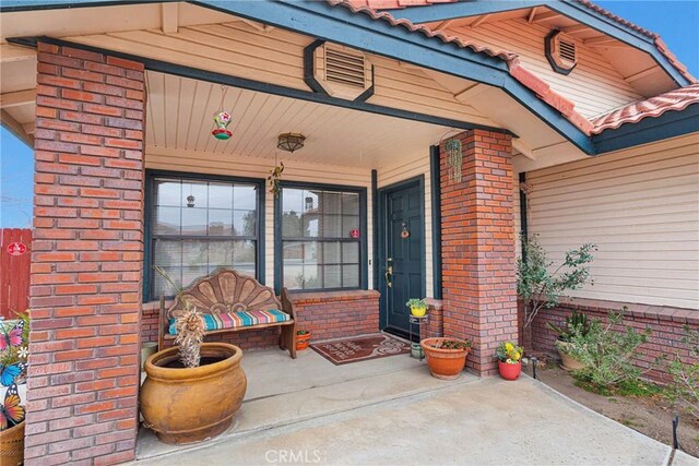 view of exterior entry with a tiled roof, brick siding, and a porch