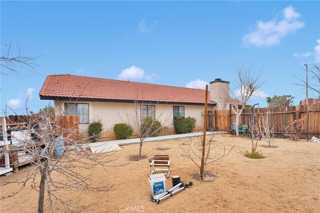 view of side of home with a tile roof, a chimney, fence, and stucco siding