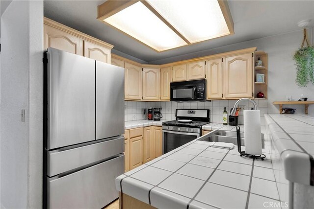 kitchen featuring light brown cabinets, appliances with stainless steel finishes, decorative backsplash, and tile counters