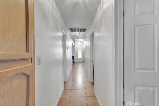 hallway featuring a textured wall, light tile patterned flooring, visible vents, and baseboards