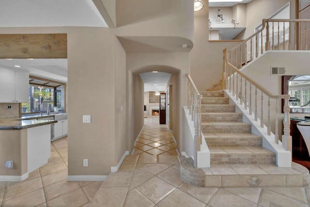 foyer featuring light tile patterned floors, baseboards, visible vents, arched walkways, and a towering ceiling