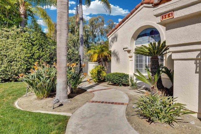 view of exterior entry with a tiled roof, fence, and stucco siding