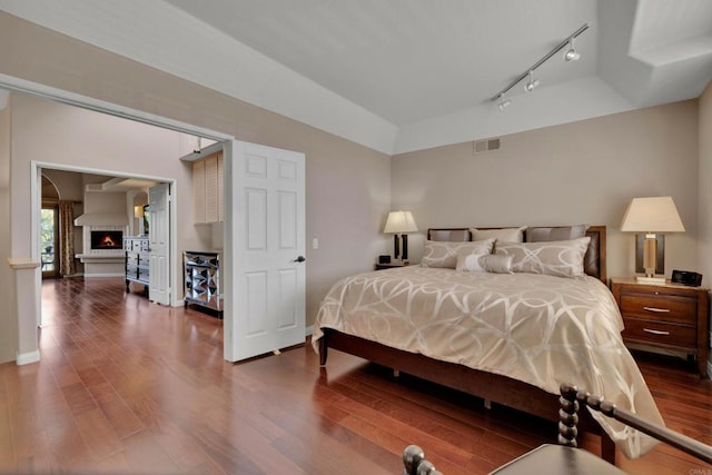 bedroom with a warm lit fireplace, dark wood-type flooring, visible vents, and baseboards