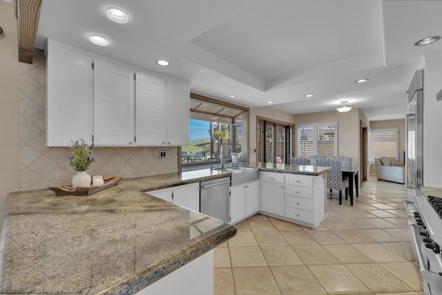 kitchen with a raised ceiling, decorative backsplash, white cabinets, appliances with stainless steel finishes, and a peninsula