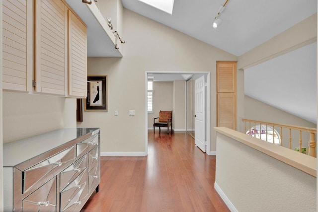 hall with vaulted ceiling with skylight, track lighting, wood finished floors, and baseboards