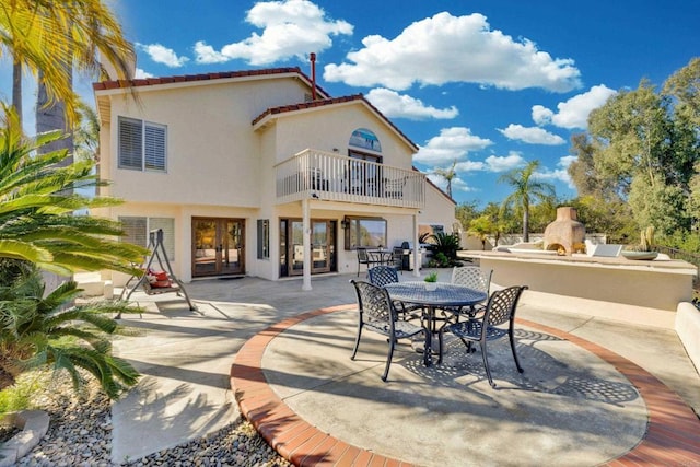 rear view of property featuring french doors, a fireplace, a patio, stucco siding, and a balcony