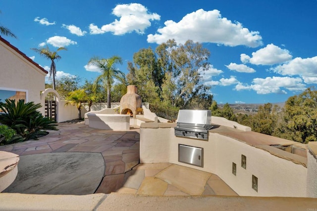 view of patio / terrace featuring a warm lit fireplace, grilling area, an outdoor kitchen, and fence