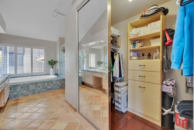 bathroom featuring lofted ceiling, vanity, a bath, tile patterned floors, and a walk in closet