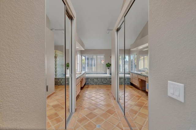 hallway with lofted ceiling, light tile patterned flooring, and a textured wall