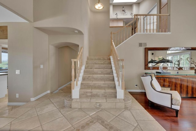 stairway featuring a high ceiling, visible vents, arched walkways, and baseboards