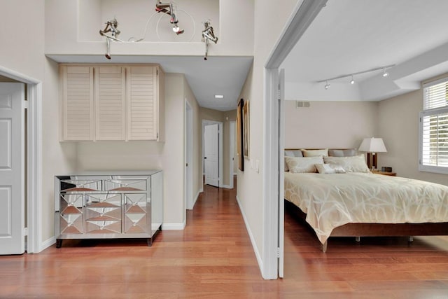 bedroom with track lighting, light wood-type flooring, visible vents, and baseboards