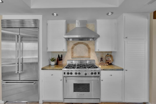 kitchen with wall chimney exhaust hood, high end appliances, visible vents, and white cabinetry