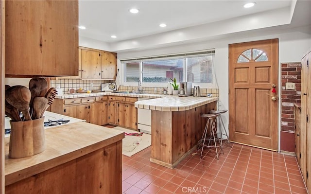 kitchen with tile countertops, white dishwasher, recessed lighting, a peninsula, and decorative backsplash