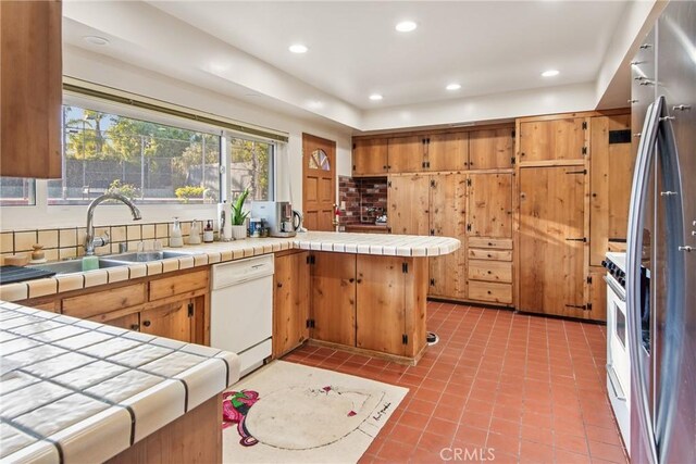 kitchen featuring dishwasher, tile countertops, a peninsula, and a sink