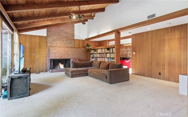 living room featuring wooden walls, carpet floors, visible vents, a brick fireplace, and beamed ceiling