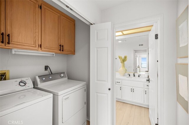 clothes washing area featuring light wood-style flooring, cabinet space, visible vents, and washing machine and clothes dryer