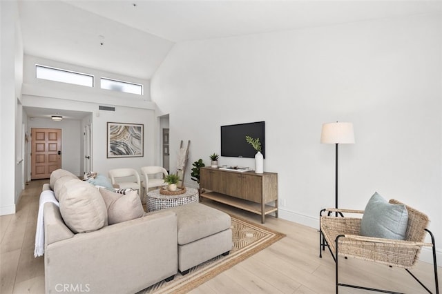 living area with light wood-style flooring, visible vents, high vaulted ceiling, and baseboards