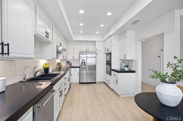 kitchen with under cabinet range hood, stainless steel appliances, a sink, light wood-type flooring, and dark countertops