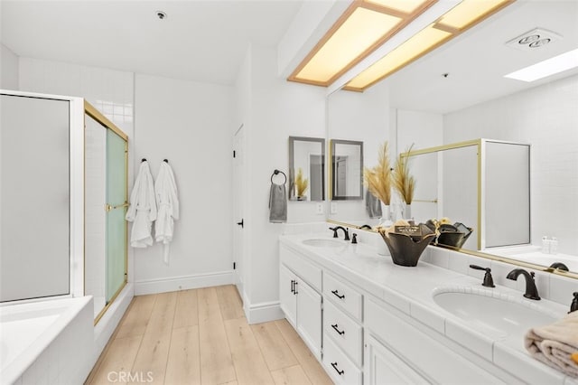 bathroom featuring double vanity, a stall shower, a sink, and wood finished floors