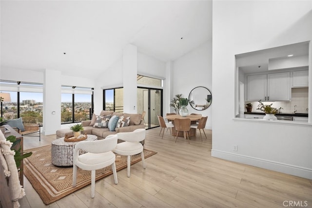 living room featuring high vaulted ceiling, light wood-type flooring, and baseboards