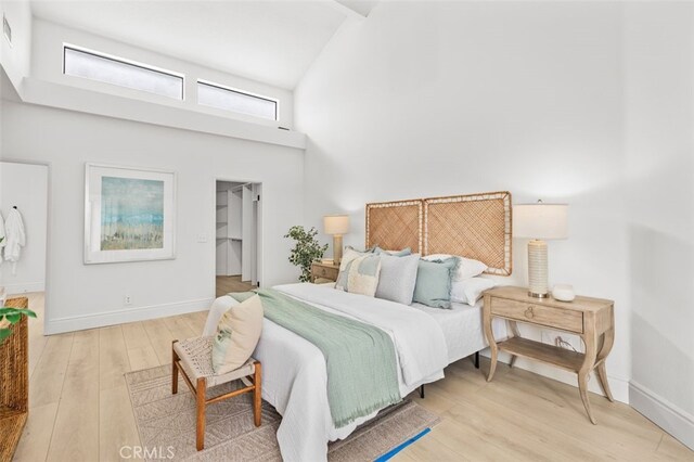 bedroom with high vaulted ceiling, wood finished floors, visible vents, baseboards, and a walk in closet