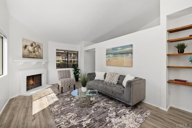 living area featuring a brick fireplace, baseboards, vaulted ceiling, and wood finished floors