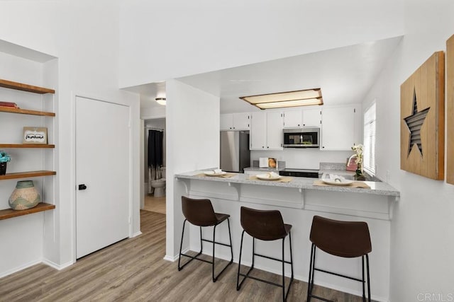 kitchen featuring stainless steel appliances, white cabinets, light wood-style floors, and a peninsula