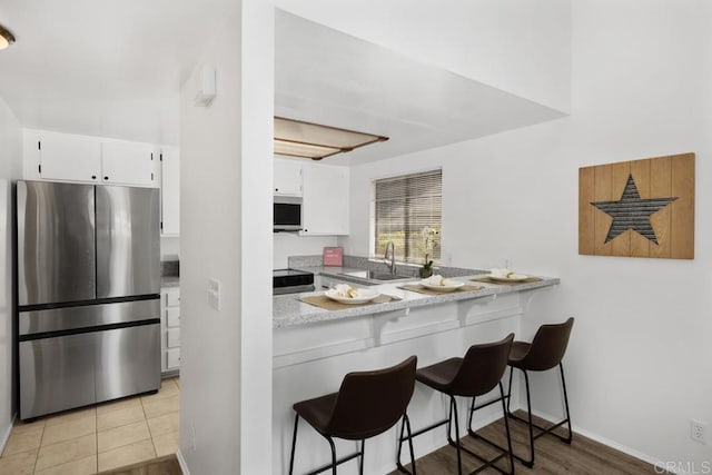 kitchen featuring stainless steel appliances, a kitchen bar, a sink, and white cabinetry