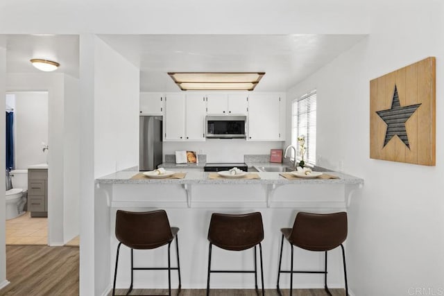 kitchen with a peninsula, appliances with stainless steel finishes, white cabinets, and a sink