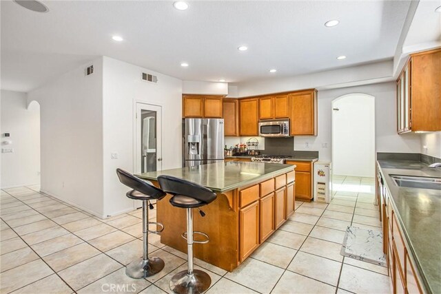 kitchen featuring brown cabinets, appliances with stainless steel finishes, arched walkways, and a sink