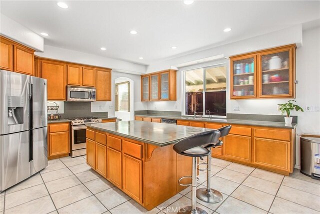 kitchen with arched walkways, light tile patterned flooring, a center island, appliances with stainless steel finishes, and brown cabinets