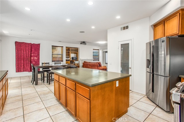 kitchen featuring visible vents, brown cabinetry, stainless steel fridge with ice dispenser, dark countertops, and a kitchen island