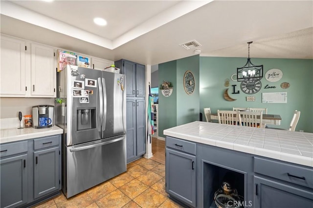 kitchen with hanging light fixtures, visible vents, tile counters, and stainless steel refrigerator with ice dispenser