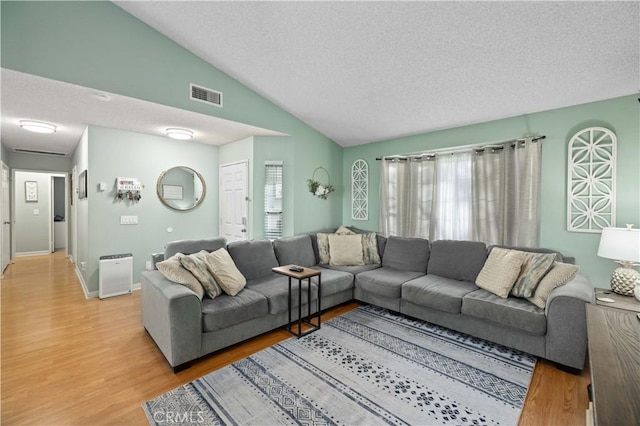 living area with lofted ceiling, a textured ceiling, visible vents, baseboards, and light wood-type flooring