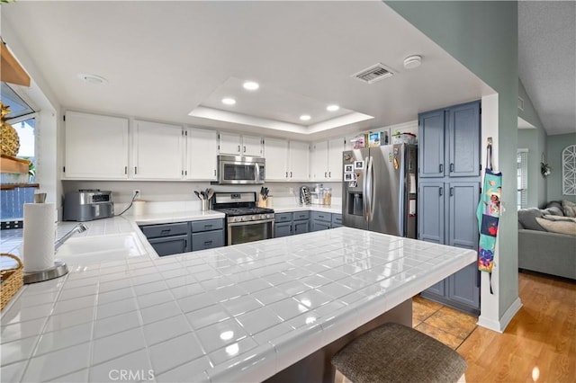 kitchen with tile countertops, stainless steel appliances, recessed lighting, a raised ceiling, and visible vents