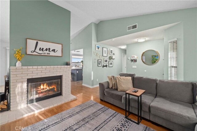 living area with a fireplace, wood finished floors, visible vents, baseboards, and vaulted ceiling