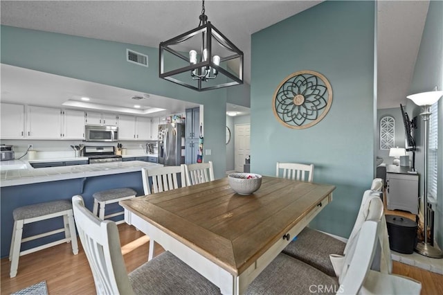 dining room with lofted ceiling, visible vents, light wood finished floors, and an inviting chandelier