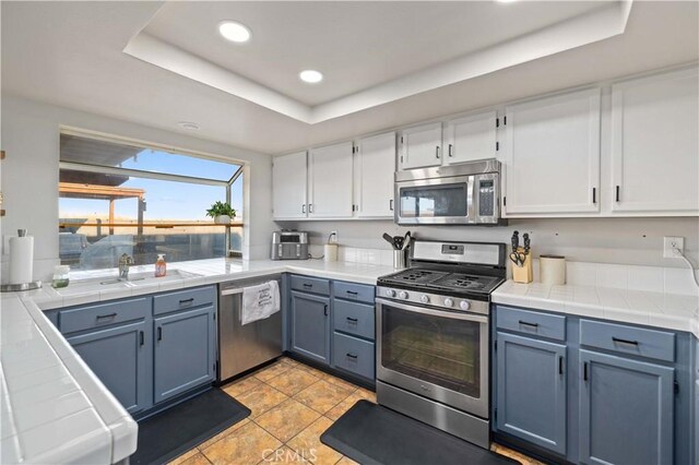 kitchen featuring appliances with stainless steel finishes, a raised ceiling, white cabinetry, and tile countertops