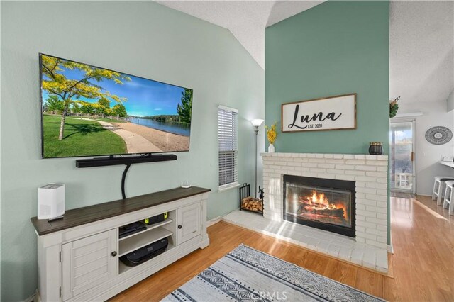 living area with a textured ceiling, a fireplace, vaulted ceiling, and wood finished floors