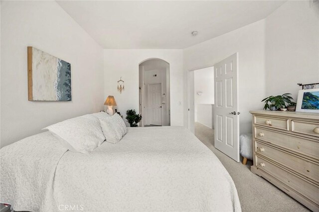 bedroom with arched walkways and light colored carpet