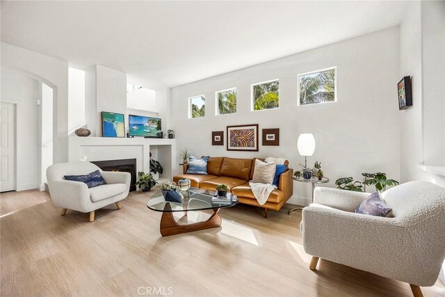 living room with arched walkways, a warm lit fireplace, wood finished floors, and a wealth of natural light